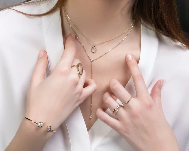 Close-up of a person wearing gold jewelry including a necklace, ring, and bracelet on a white background.